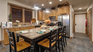 A kitchen with wooden cabinets, a granite countertop, a stainless steel refrigerator, and a dining area with a marble table and wooden chairs.