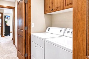 A laundry room with a washer and dryer, wooden cabinets, and a hallway leading to another room.