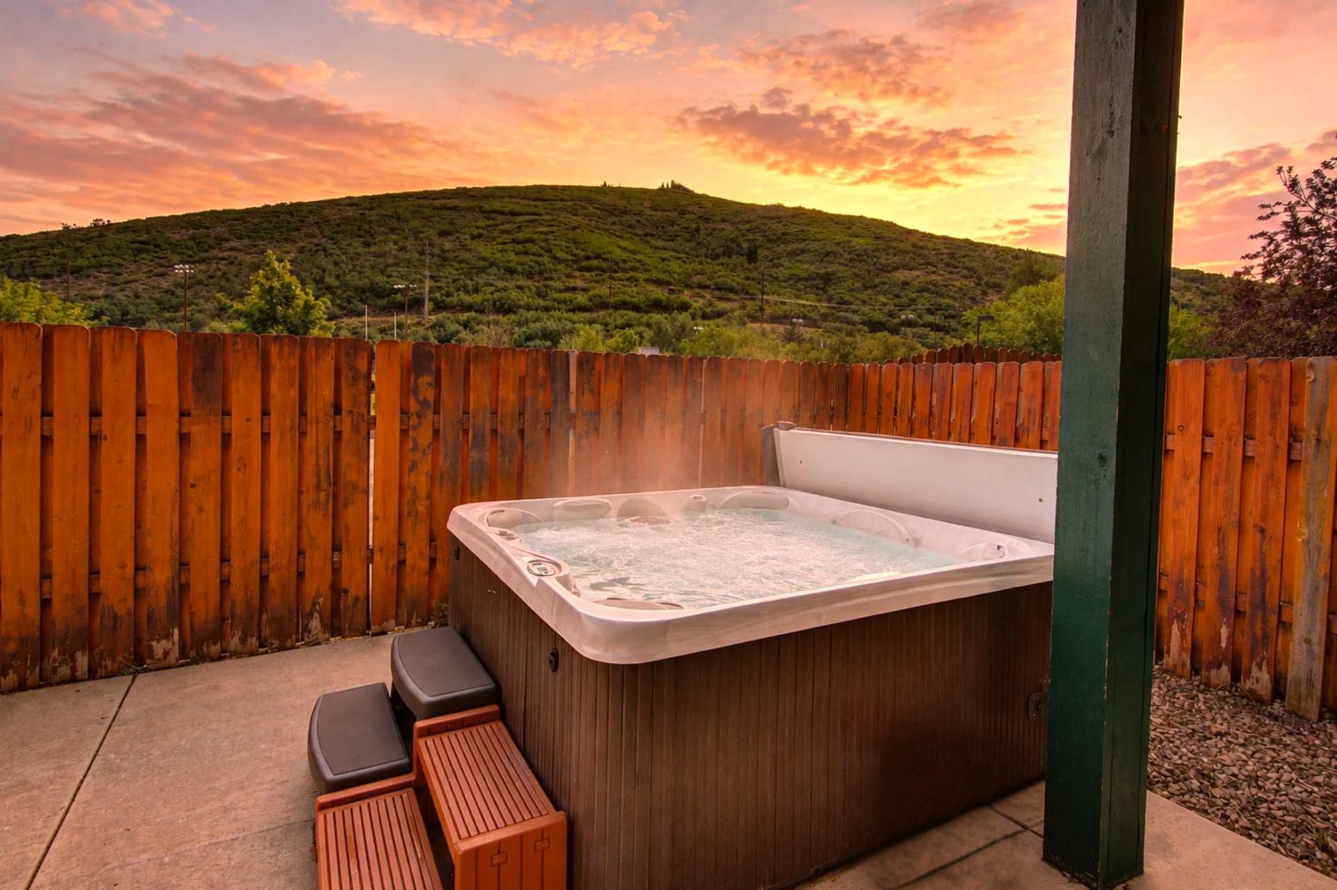 A hot tub with steps in a wooden-fenced outdoor area with a view of a hill.