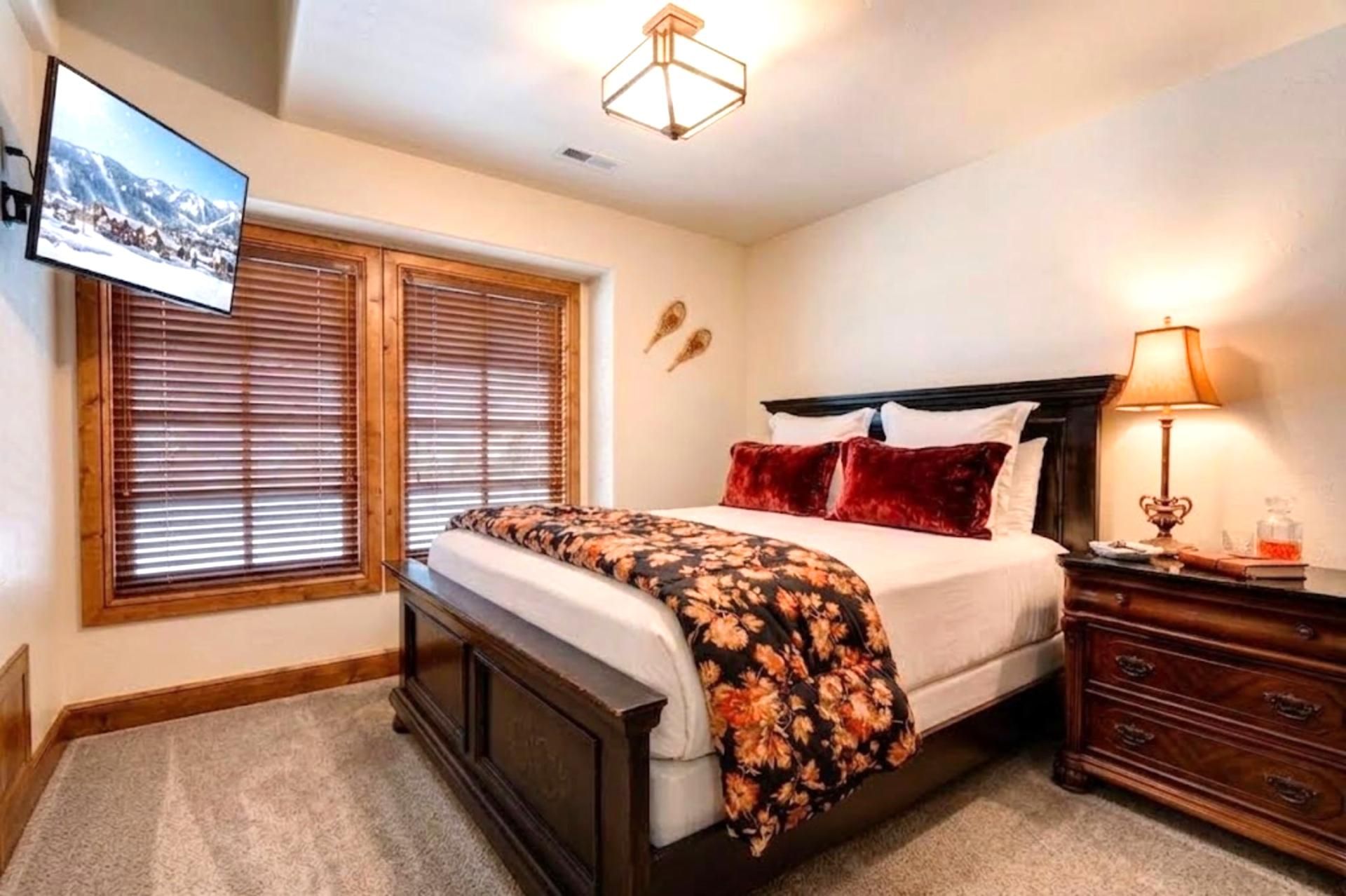 A bedroom with a bed, a bedside table with a lamp, a dresser, and a wall-mounted TV.
