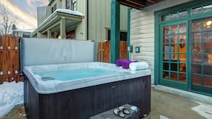 A hot tub in a backyard with a wooden fence, a wooden deck, and a green door.