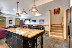 Una cocina amplia con isla de granito, iluminación colgante y un comedor con sillas y una mesa.