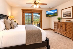 A bedroom with a large bed, a ceiling fan, a dresser, and a TV on the wall.