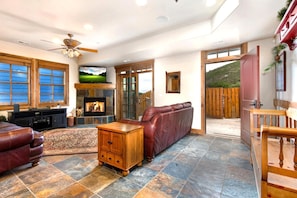 A spacious living room with a fireplace, leather sofa, and a television mounted above it.