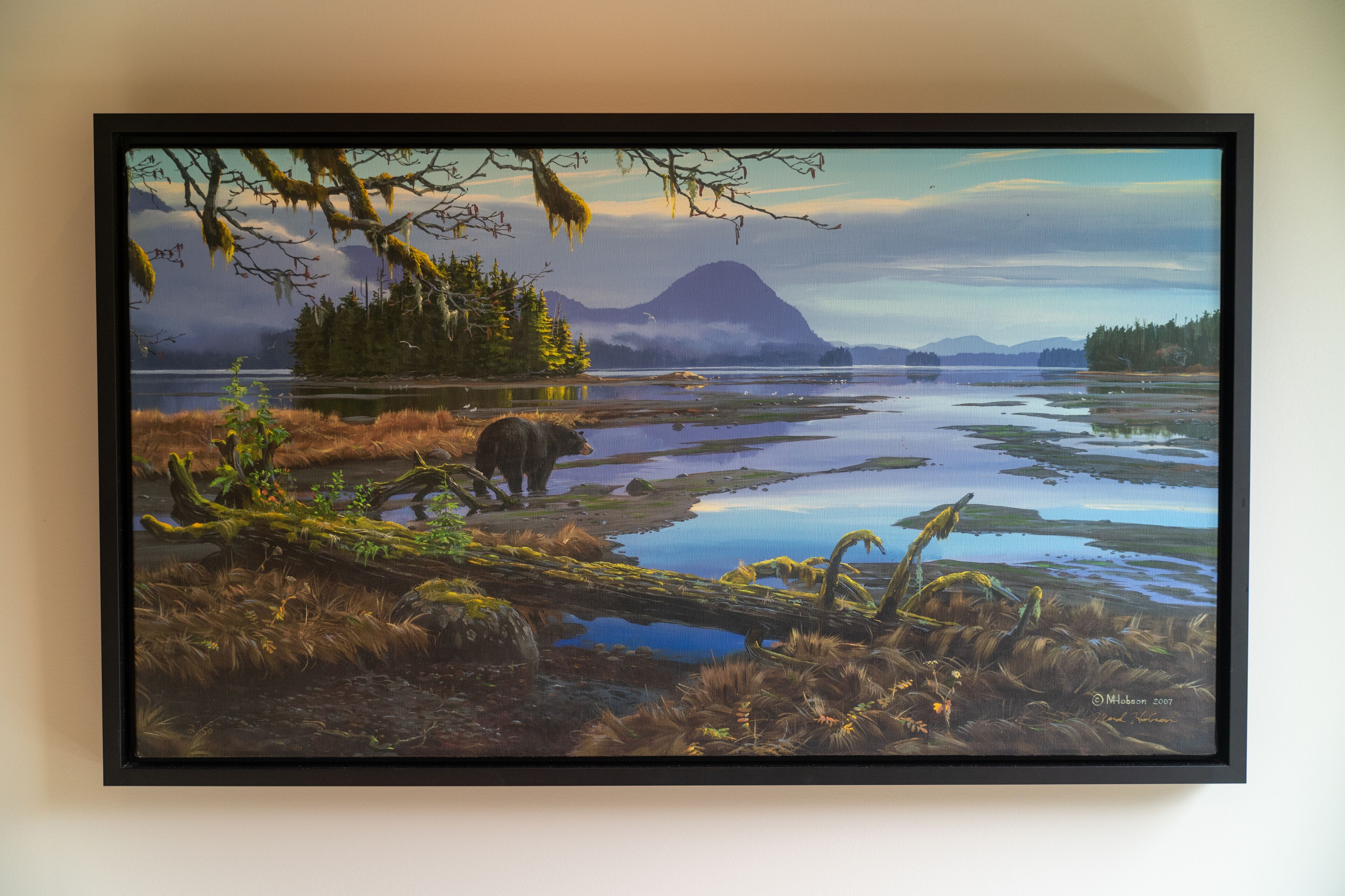 Un tableau représentant un paysage, encadré, avec un ours, des arbres et une montagne.