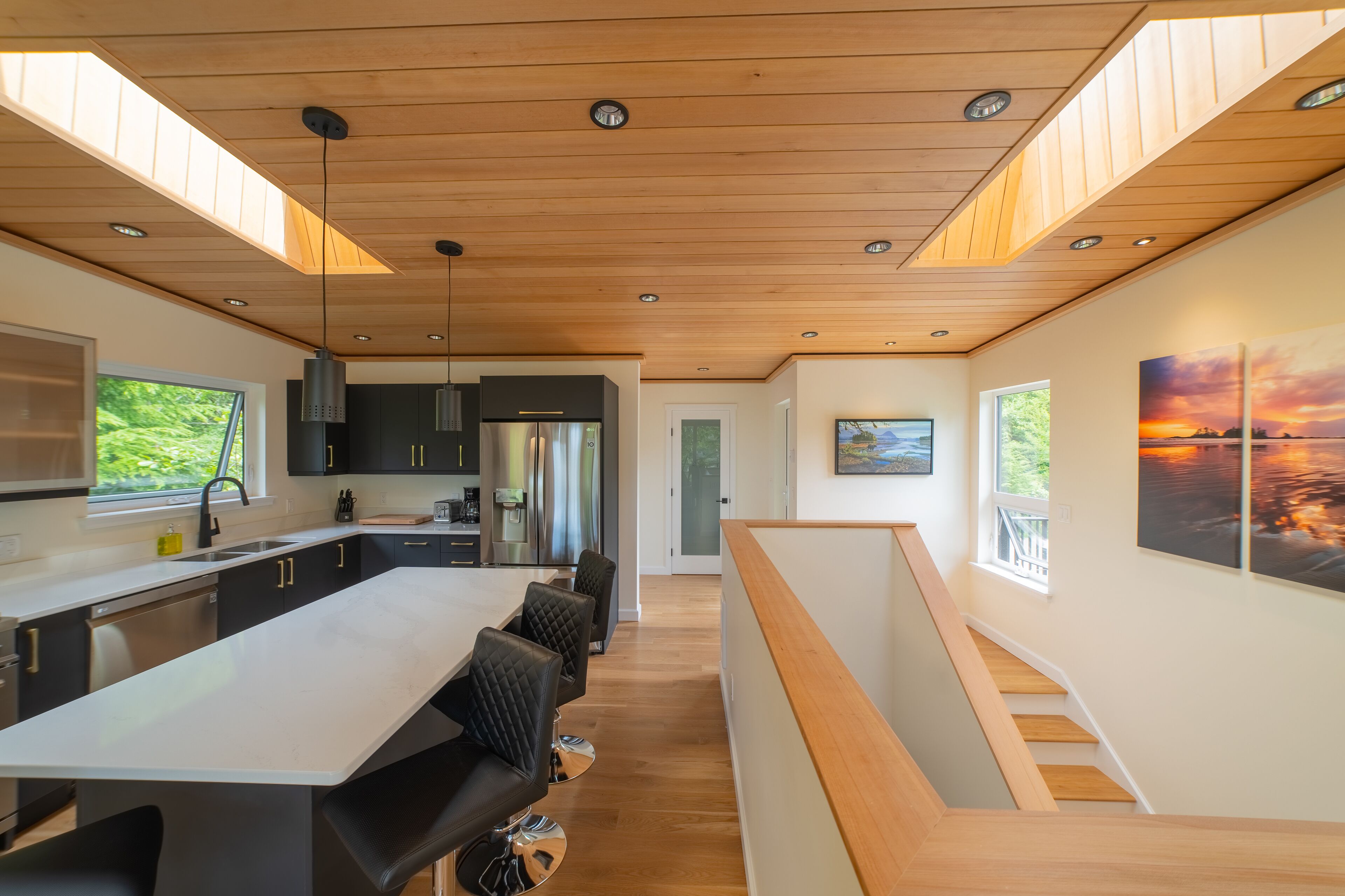 Una cocina moderna con una isla central, muebles negros, electrodomésticos de acero inoxidable y techo de madera.