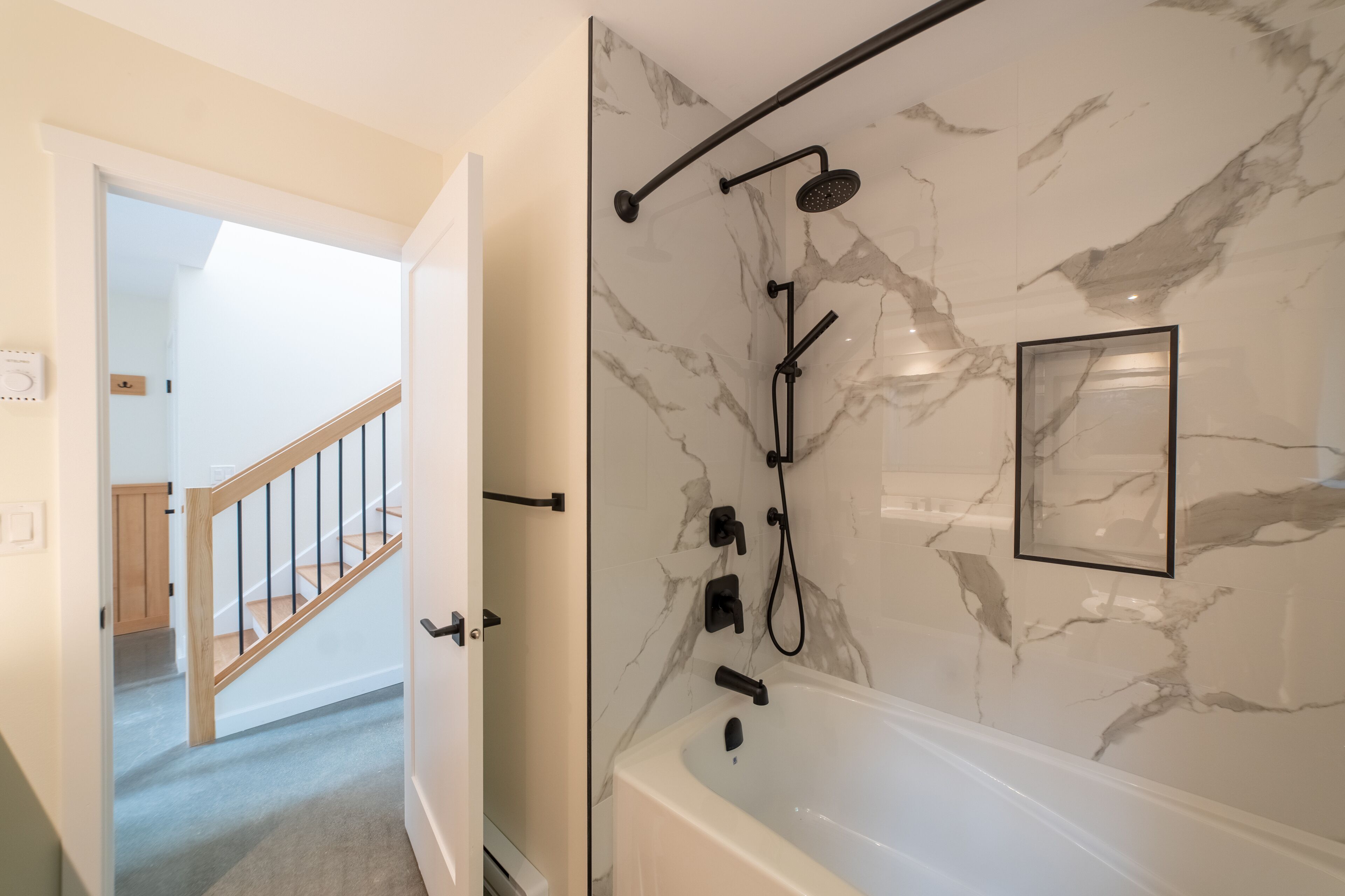 A bathroom with a marble wall, a bathtub, and a shower with a handheld showerhead.