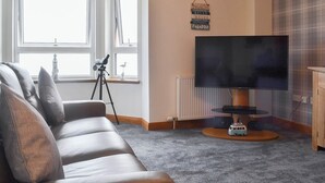 Olohuoneessa on sohva, kaukoputki, jalustalla oleva televisio ja seinällä oleva kyltti.