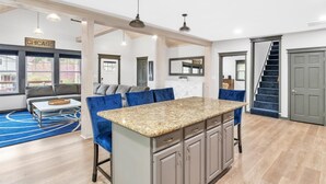 A spacious kitchen with a central island, a dining area with blue chairs, and a staircase leading to a second floor. - Contemporary, cozy,  hidden gem close to wineries (Buchanan)