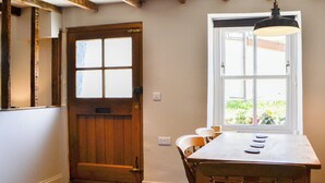 Een eetgedeelte met een houten tafel en stoelen, een raam met uitzicht op groen, en een houten deur met een mat met stermotief.