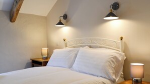 Een opgemaakt bed met witte lakens in een kamer met schuine plafonds en twee wandlampen.