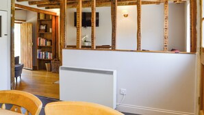 Een kamer met zichtbare houten balken, een witte radiator, een boekenkast en een aan de muur bevestigde televisie.