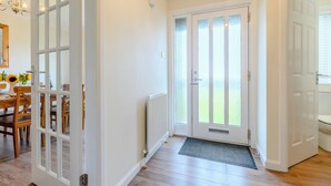 A hallway with a wooden floor, a dining area with a table and chairs, and a door leading to a balcony. - 4 bedroom accommodation in Beadnell (Beadnell)