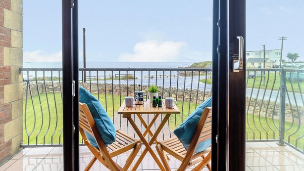 A balcony with a table and chairs, a view of the sea, and a stone wall. - 4 bedroom accommodation in Beadnell (Beadnell)