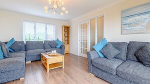 A living room with two grey sofas, a wooden coffee table, and a chandelier. - 4 bedroom accommodation in Beadnell (Beadnell)