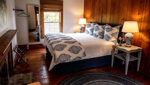 A bedroom with a wooden paneled wall, a bed with patterned bedding, two bedside lamps, a small table with a vase, and a wooden bench.