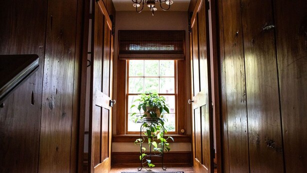 A wooden hallway with a large window, a potted plant, and a patterned rug.
