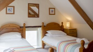 Un dormitorio acogedor en el ático con dos camas de madera, un espejo y una mesita de noche con una lámpara.