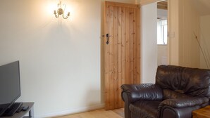 Una habitación con puerta de madera, sofá de cuero, televisor sobre un mueble bajo y una lámpara fijada a la pared.