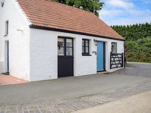 A white building with a red-tiled roof, a blue door, and a black gate.