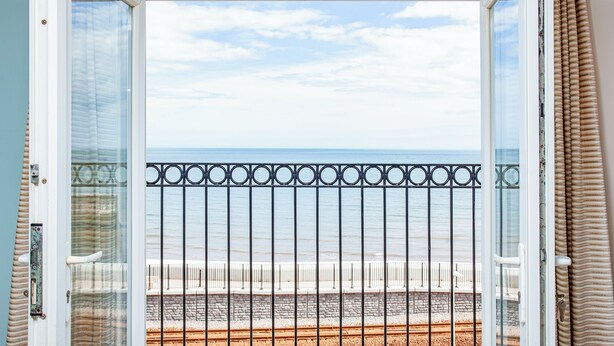 Un balcon doté d’une balustrade en métal, donnant sur une plage et une voie ferrée.