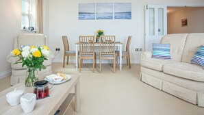 Un salon comprenant un canapé, une table à manger avec des chaises et une table basse ornée d’un vase de fleurs et de tasses à thé.