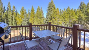 Eine Holzterrasse mit Grill, Tisch und vier Stühlen.