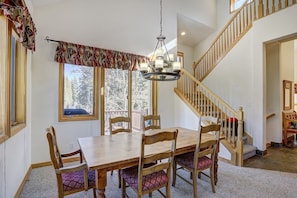 A dining area with a wooden table and chairs, a chandelier, and a staircase.