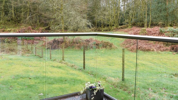 A view from a balcony with a glass railing overlooking a grassy area with trees and a fence. - 2 bedroom accommodation in near Windermere (near Windermere)