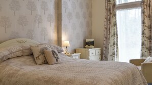 A bedroom with a large bed, a nightstand with a lamp, a bedside table with a book, and a window with curtains. - 2 bedroom accommodation in near Windermere (near Windermere)