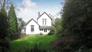 A two-story white house with a sloped roof, surrounded by lush greenery and trees. - 2 bedroom accommodation in near Windermere (near Windermere)