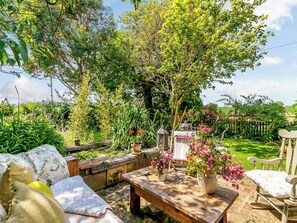 A garden patio with wooden furniture, potted plants, and a stone wall.