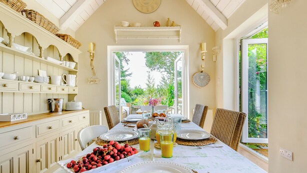A dining room with a table set for four, a bowl of cherries, a pitcher of juice, and a view of the garden through the open door. - Beautiful house, peaceful surrounding yet close to towns and beaches. (Faversham)