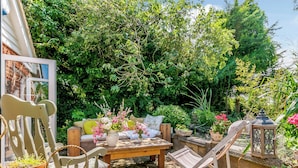 A garden patio with a wooden bench, a chair, and a table with potted plants. - Beautiful house, peaceful surrounding yet close to towns and beaches. (Faversham)