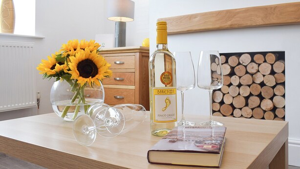 Ein Holztisch mit einer Flasche Barefoot Pinot Grigio, zwei Weingläsern, einem Buch und einer Vase mit Sonnenblumen.