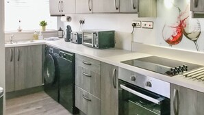 Eine moderne Küche mit grauen Schränken, einem Geschirrspüler, einer Mikrowelle und einem Backofen. Ein Fenster mit Jalousien und ein kleiner Topf mit Pflanze auf der Arbeitsfläche.