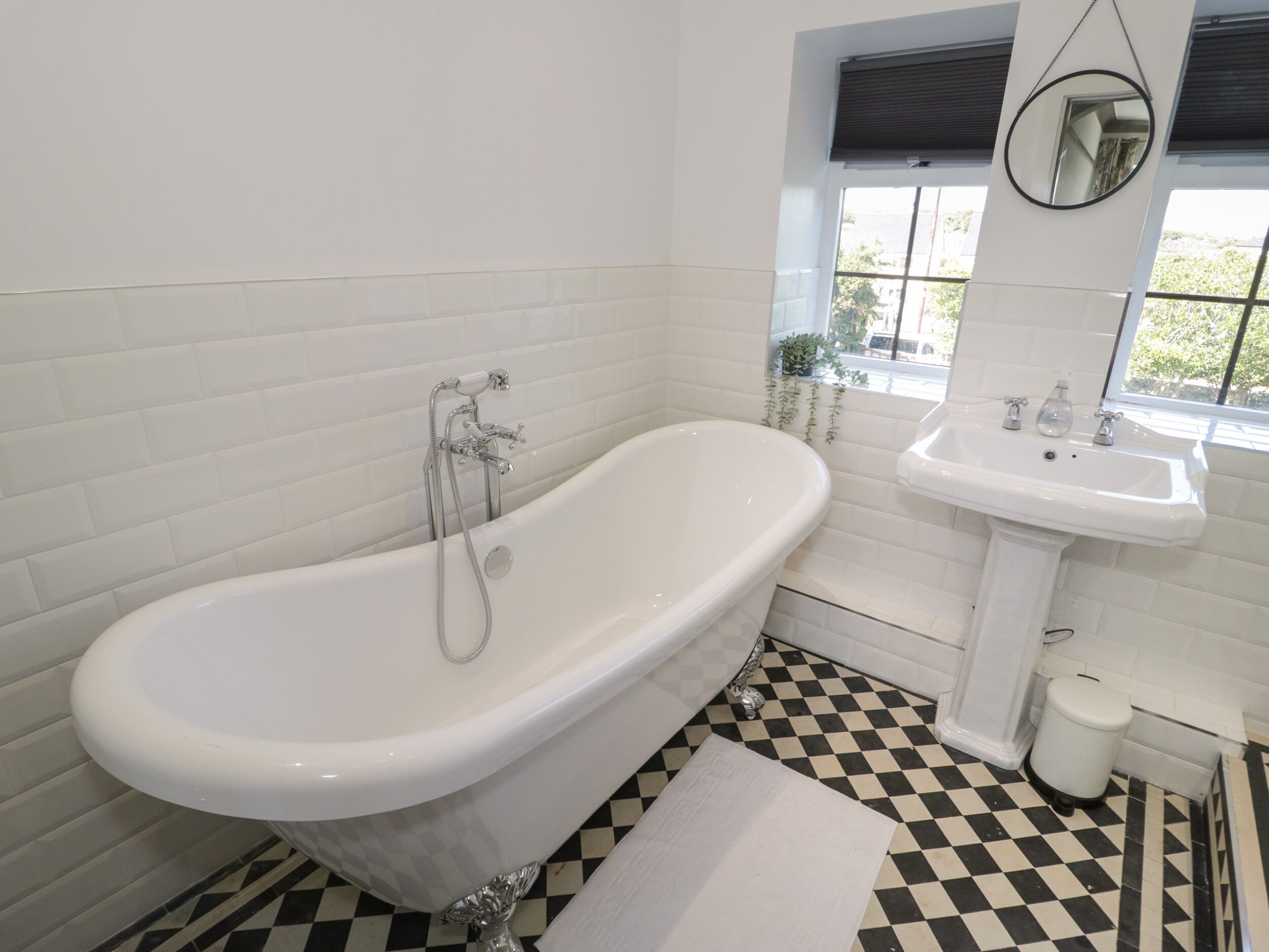 Un bagno con una vasca freestanding, un lavabo su piedistallo e una finestra con vista sul verde.