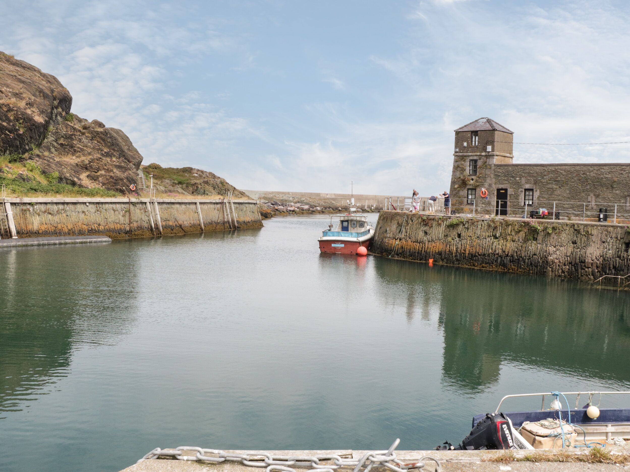 A calm harbor with a boat docked near a stone building with a tower.