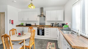 Una cocina moderna con armarios blancos, una campana extractora de acero inoxidable y una mesa de comedor de madera con sillas.