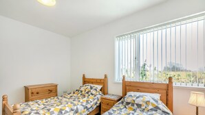Un dormitorio con dos camas de madera, una mesita de noche, una lámpara y una ventana con persianas.