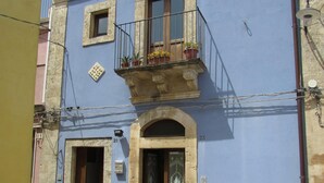 A two-story building with a blue facade, a balcony with potted plants, and a cobblestone street. - SR-G267-LENZ21A1 - Dimora Il Balcone Barocco (Palazzolo Acreide)