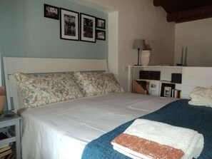 Une chambre à coucher avec un lit, une table de chevet, une lampe, une bibliothèque et des tableaux encadrés accrochés au mur.