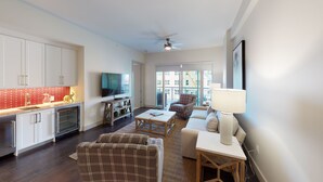 A modern living room with a flat-screen TV, a sofa, a coffee table, and a dining area with a red-tiled backsplash. - Located 200 feet from the stadium, WestGate is in the Center of Alabama football (Tuscaloosa)