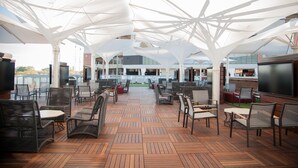 An outdoor patio area with wooden flooring, wicker furniture, and white canopies providing shade. - Located 200 feet from the stadium, WestGate is in the Center of Alabama football (Tuscaloosa)