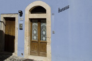 Um edifício com fachada azul, porta de madeira com painel de vidro e placa com o número 23.