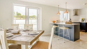 A modern kitchen with a central island, a dining area with a table set for two, and a view through large sliding doors to an outdoor area.