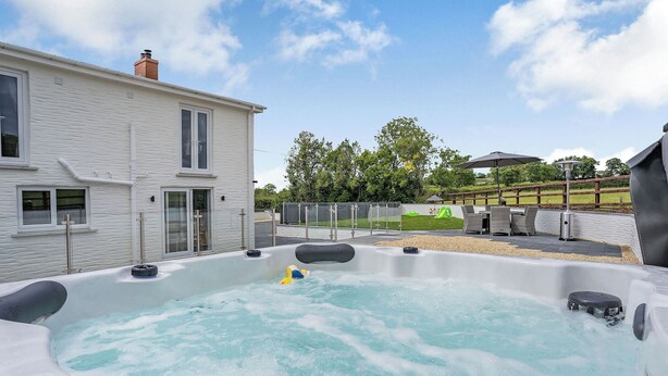 A hot tub area with a house in the background, a grassy area, and a wooden fence.