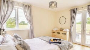 A bedroom with a bed, curtains, a bedside table with towels, a dresser, and a view of the outdoors.
