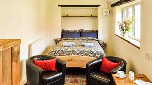 A small, cozy room with a bed, two leather chairs, a wooden table with a white pitcher and cup, and a window with a plant. - 1 bedroom accommodation in Great Hockham, near Thetford (Great Hockham, near Thetford)