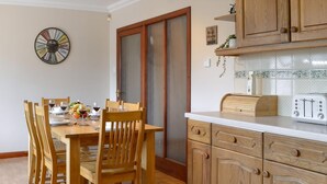 Un comedor con sillas de madera y una mesa lista para una comida, una cocina con armarios de madera y un tostador, y un reloj de pared.